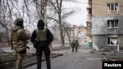 Local residents walk an empty street as police officers look at in Bakhmut